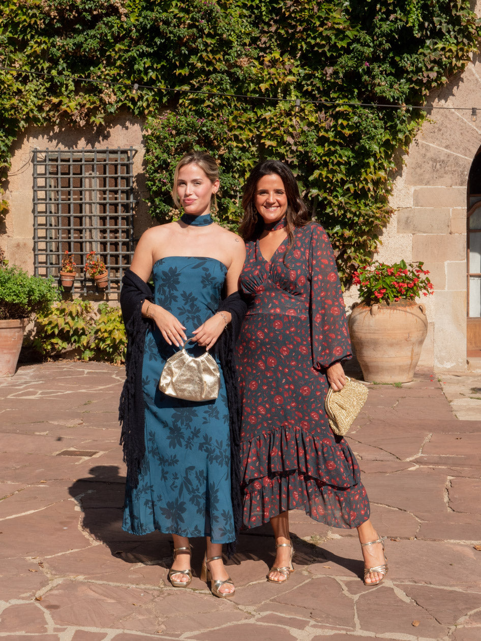 Dos invitadas con vestidos estampados, chal y bolsos dorados